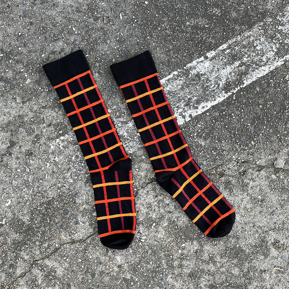 Made in USA men's black cotton geometric socks with oranges, yellows, and reds in a windowpane plaid/grid pattern by THIS NIGHT